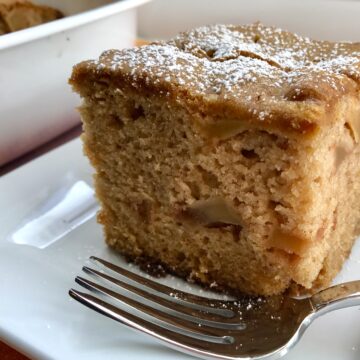 Slice of the Best Apple Cinnamon Cake on a plate with a fork. When you bake this cake, the entire house fills with the amazing aroma of cinnamon and apples. And then when you eat it, every bite gives you sweet cinnamon spice with a beautifully spongy texture and a sweet and tart pop from the apples.
