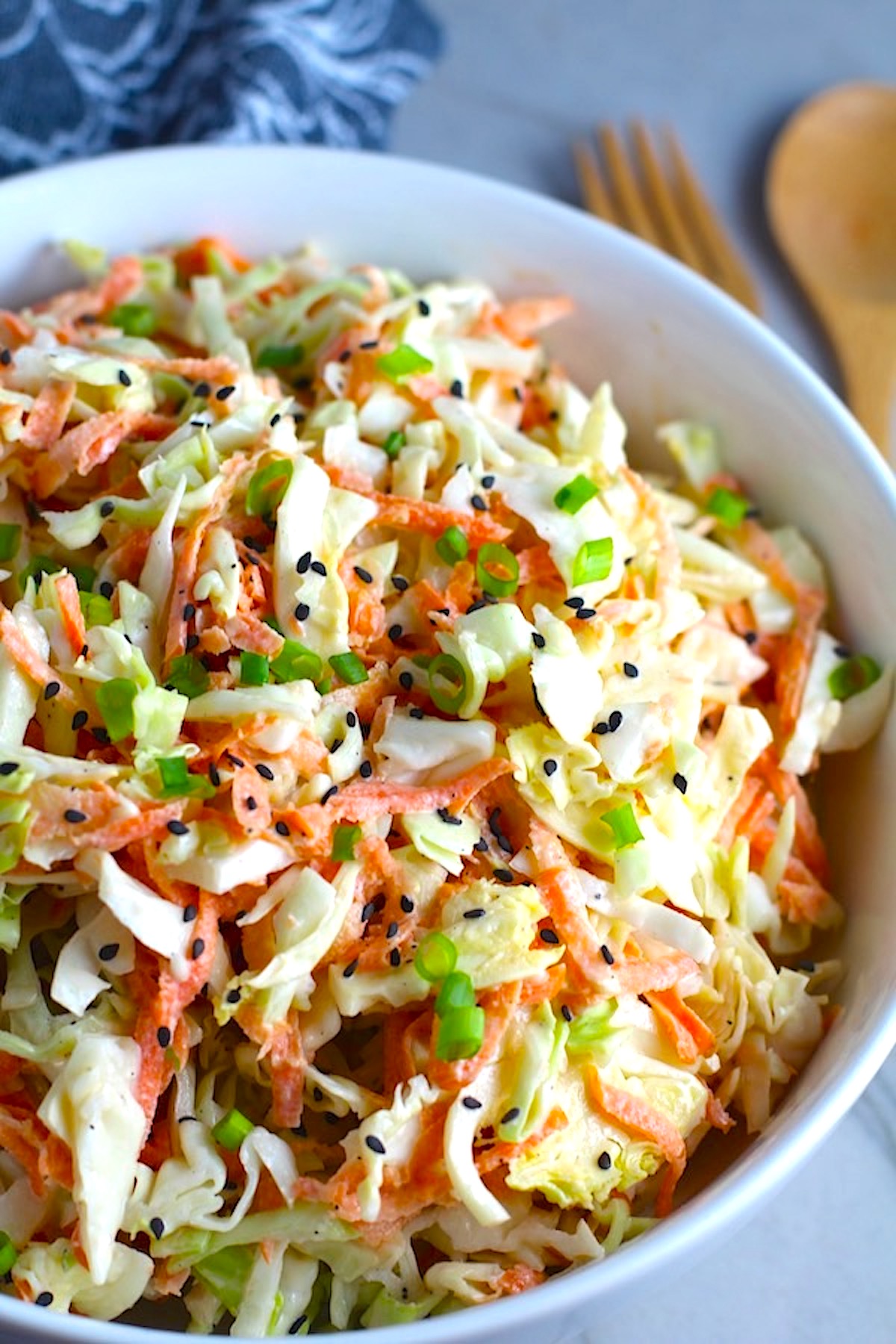 Coleslaw with an asian salad dressing recipe and black sesame seeds on top in a bowl. It has cabbage, carrots, scallions, and sesame seeds in a creamy dressing with mayonnaise. vinegar, soy sauce, and Sesame Oil. It really is a sidekick that can go with anything!