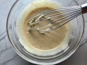 Asian Dressing with whisk in bowl for Asian Coleslaw. It has cabbage, carrots, scallions, and sesame seeds in a creamy dressing with mayonnaise. vinegar, soy sauce, and Sesame Oil. It really is a sidekick that can go with anything!