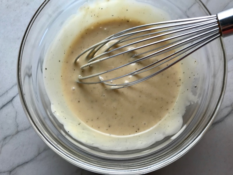 Asian Dressing with whisk in bowl for Asian Coleslaw. It has cabbage, carrots, scallions, and sesame seeds in a creamy dressing with mayonnaise. vinegar, soy sauce, and Sesame Oil. It really is a sidekick that can go with anything!