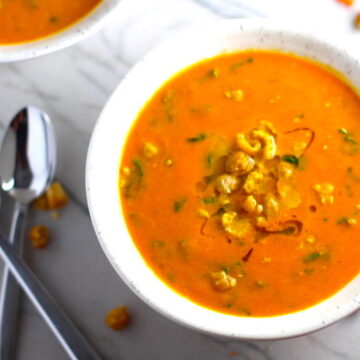 Carrot and Chickpea Soup close up in a bowl with a another bowl in back. Creamy Carrot Soup with Kale, Roasted Chickpeas and Thyme is a creamy, textured, easy-to-make soup! It's great as a starter, but hearty enough to be a meal with Kale and Chickpeas. Not only does this soup taste delicious, it's also incredibly healthy with vitamins, nutrients, fiber, and protein!
