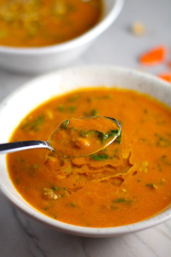 Carrot Soup close up with spoon in a bowl with a another bowl in back. Creamy Carrot Soup with Kale, Roasted Chickpeas and Thyme is a creamy, textured, easy-to-make soup! It's great as a starter, but hearty enough to be a meal with Kale and Chickpeas. Not only does this soup taste delicious, it's also incredibly healthy with vitamins, nutrients, fiber, and protein!