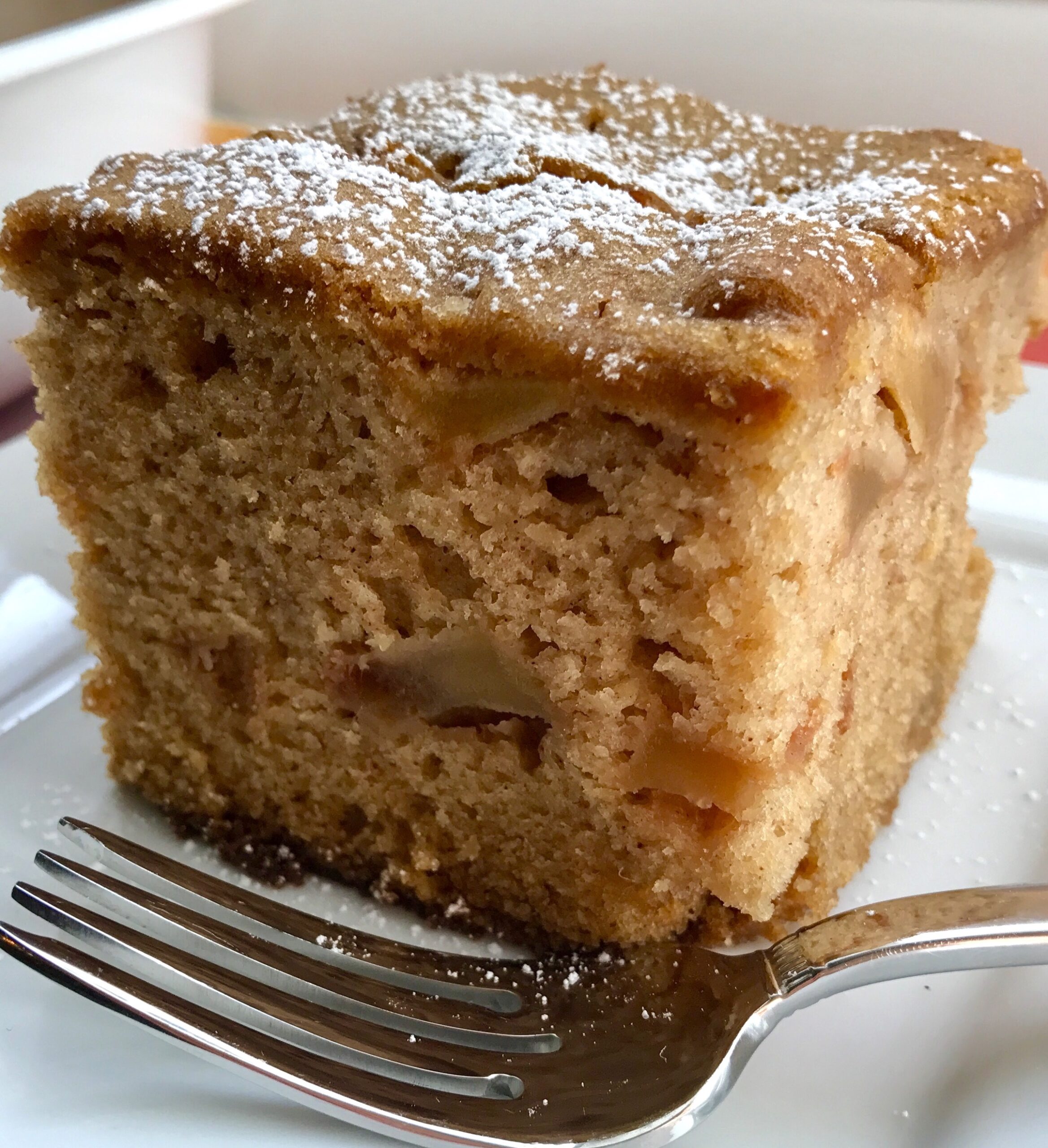 Slice of the Best Apple Cinnamon Cake on a plate with a fork. When you bake this cake, the entire house fills with the amazing aroma of cinnamon and apples. And then when you eat it, every bite gives you sweet cinnamon spice with a beautifully spongy texture and a sweet and tart pop from the apples.