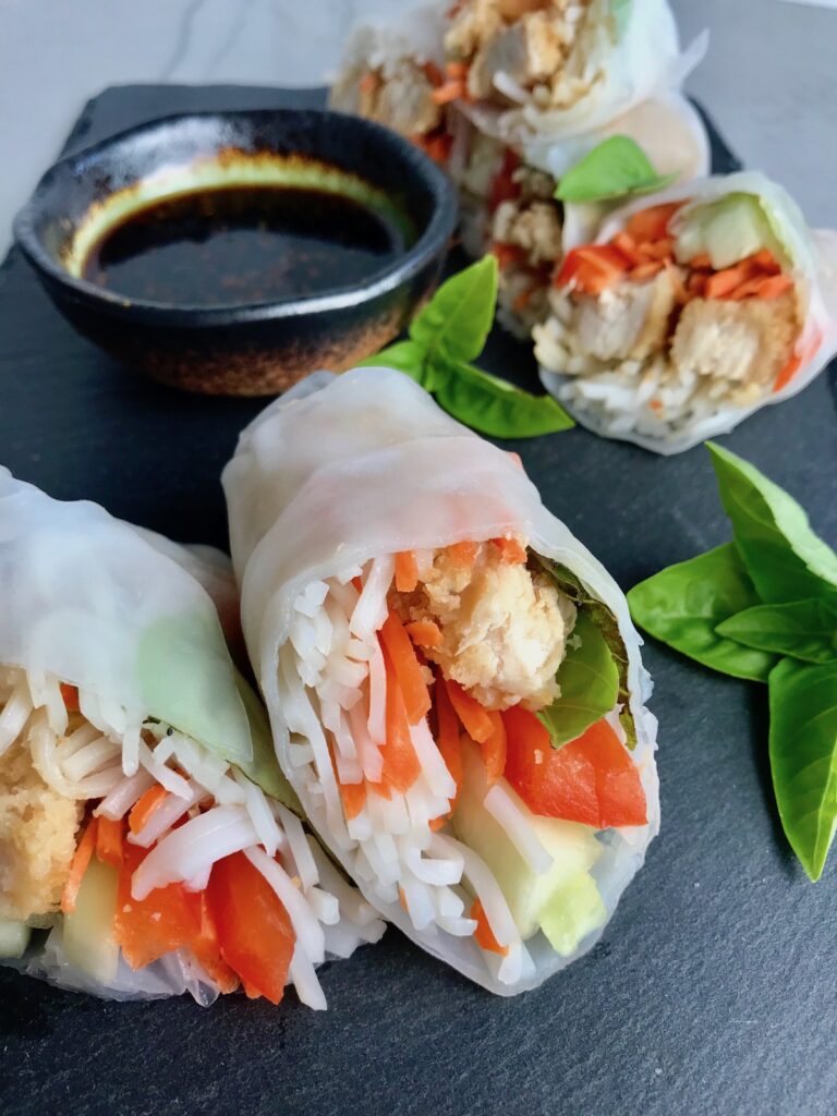 Teriyaki Chicken Summer Rolls with carrots, basil, red pepper and rice noodles inside, cut in half and stacked on slate platter with Garlic Honey Soy Dipping Sauce. Easy, fun, and delicious!