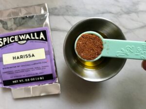 Adding Harissa powder to olive oil with package of Harissa on counter for Edamame Dip with Gorgonzola. It's creamy, savory, nutty, and utterly delicious!