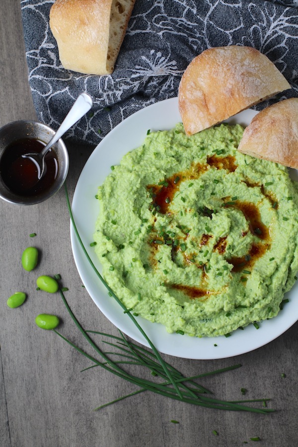 Edamame Dip with Gorgonzola and Harissa Oil drizzled on top on a plate with bread. It's creamy, savory, nutty, and utterly delicious!