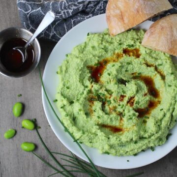 Edamame Dip with Gorgonzola and Harissa Oil drizzled on top on a plate with bread. It's creamy, savory, nutty, and utterly delicious!