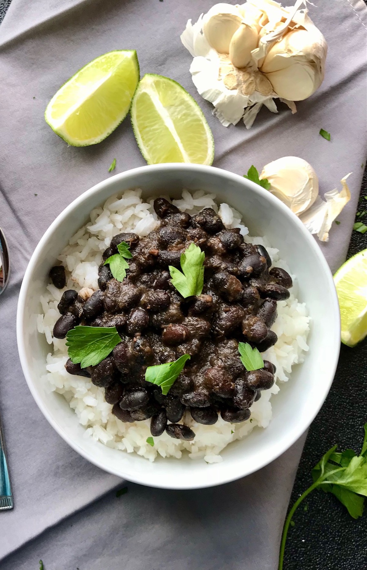 Slow Cooker Brazilian Beans and rice in a bowl with cilantro on top and lime wedges on the counter. These black beans are thick, rich, and delicious! Serve as a side or main over rice.