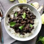 Slow Cooker Brazilian Beans and rice in a bowl with cilantro on top and lime wedges on the counter. These black beans are thick, rich, and delicious! Serve as a side or main over rice.