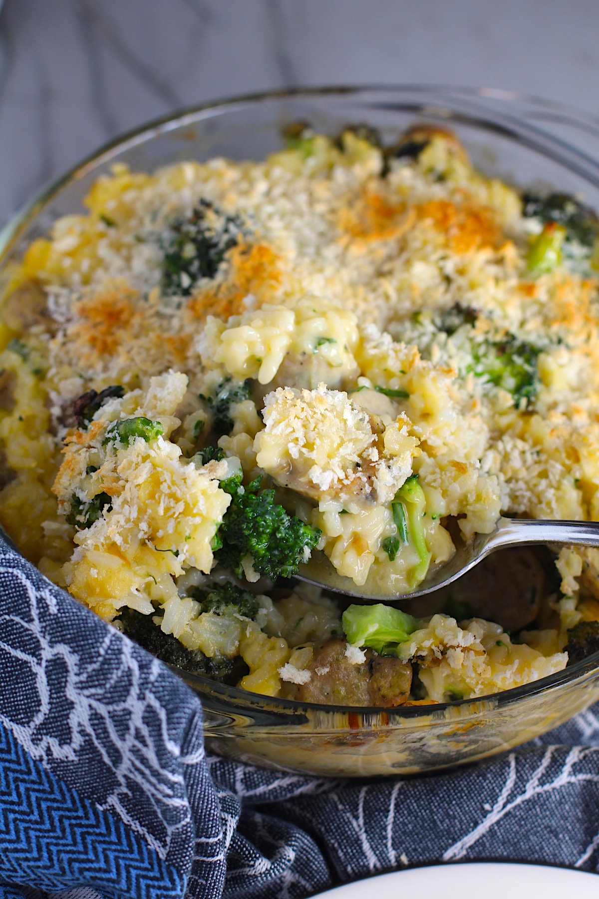 Cheesy Chicken and Broccoli Rice Casserole with bread crumb topping in casserole dish being scooped out with a spoon.