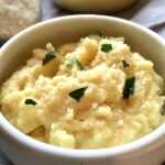 Creamy Parmesan Polenta in a bowl with parsley on top and serving bowl of polenta in background.