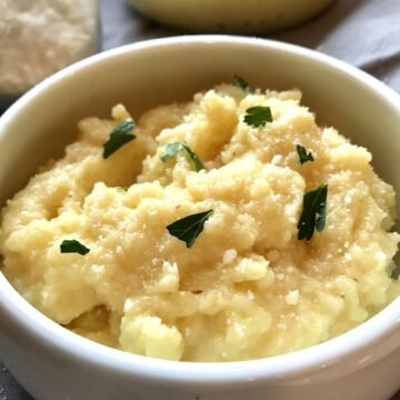 Creamy Parmesan Polenta in a bowl with parsley on top and serving bowl of polenta in background.