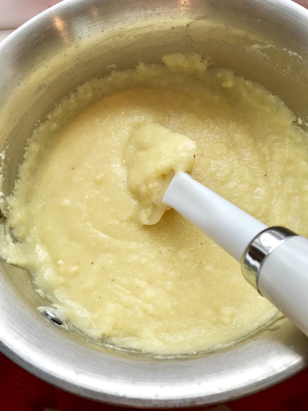 Spatula stirring Creamy Parmesan Polenta in a saucepan.