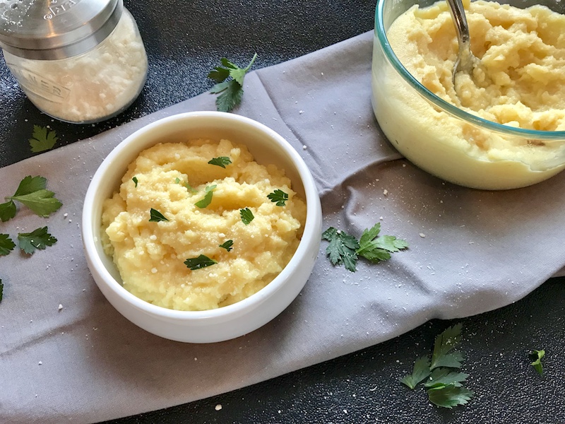 Creamy Parmesan Polenta in a bowl with parsley on top and serving bowl of polenta in background.