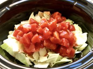 Raw cabbage and diced tomatoes in a crockpot insert for Detox Cabbage Soup.