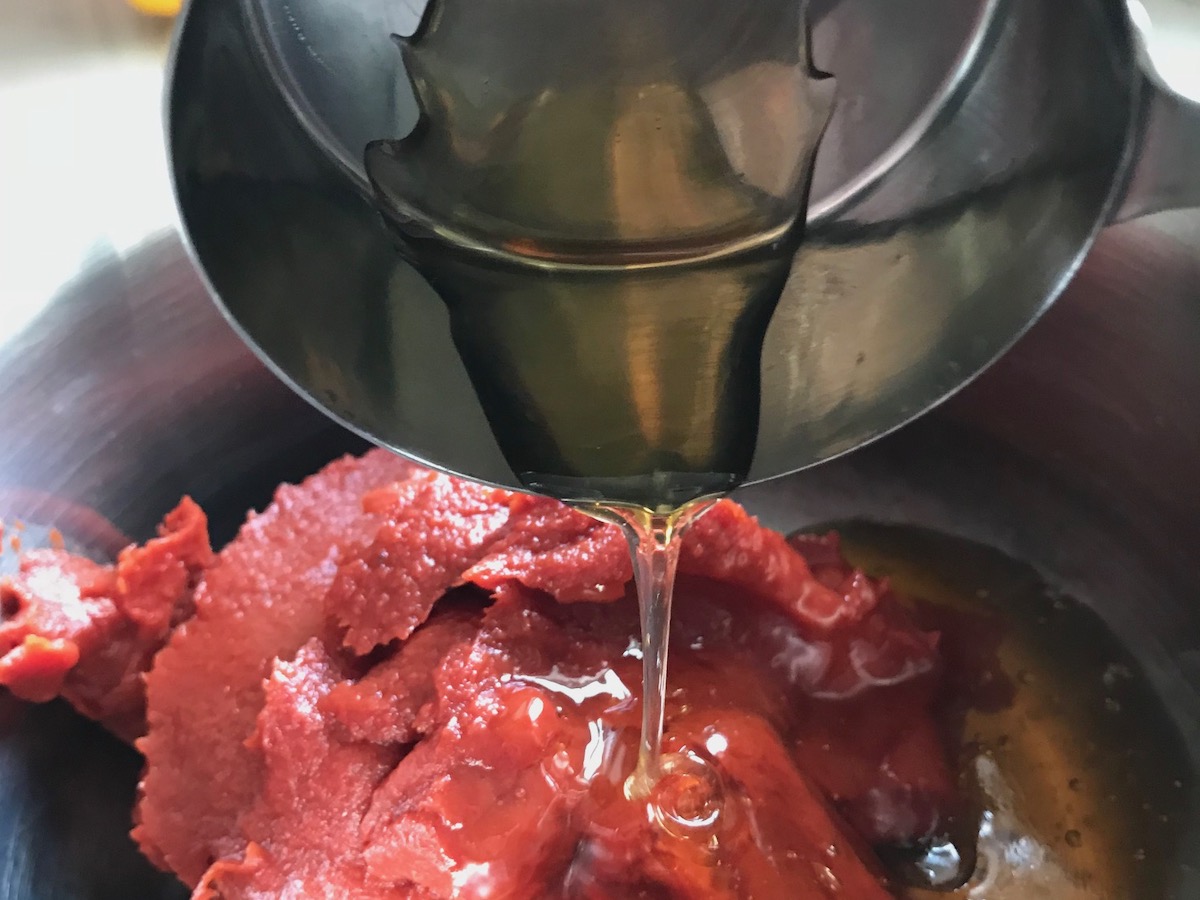 Honey pouring over tomato paste in pot for the Best Honey Ketchup recipe.