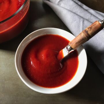 Homemade Honey Ketchup in a white serving bowl with spreading knife and large bowl of ketchup in background.