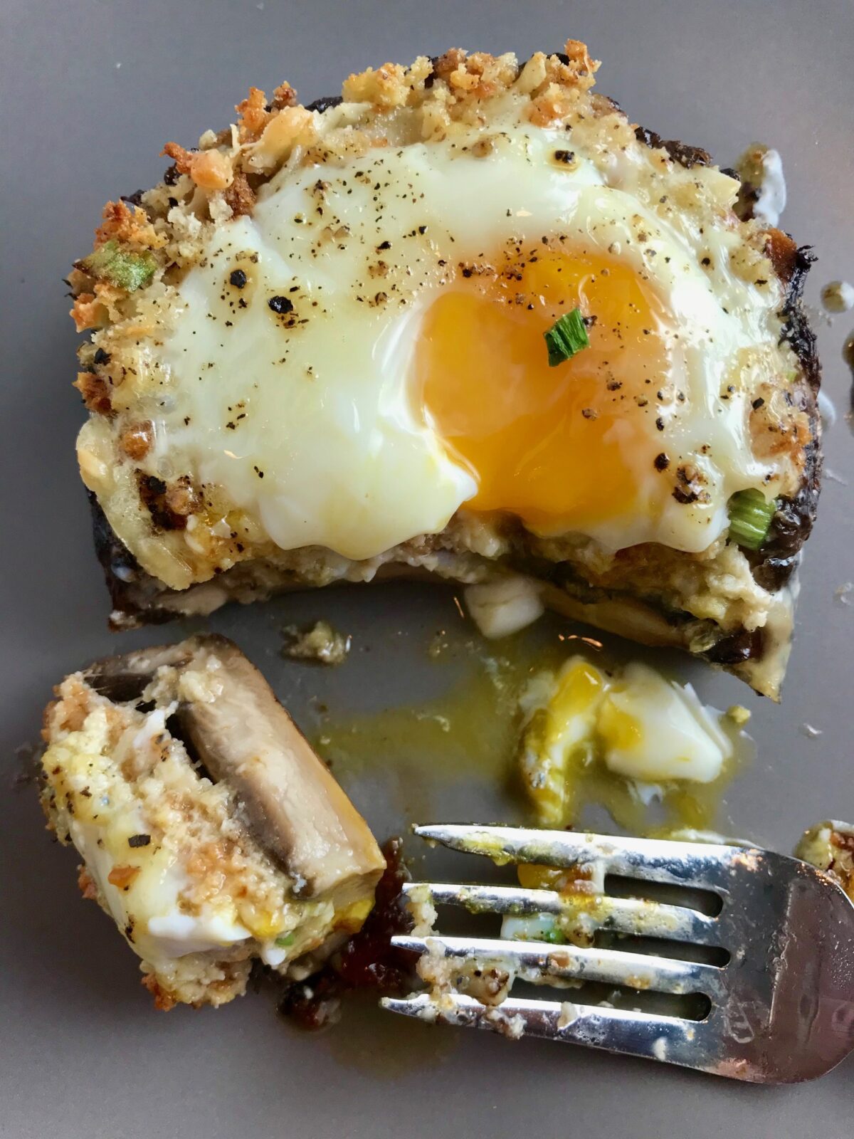 Breakfast Stuffed Mushrooms, portabella Egg Nest, on plate with bite cut out and runny yoke and fork on plate.