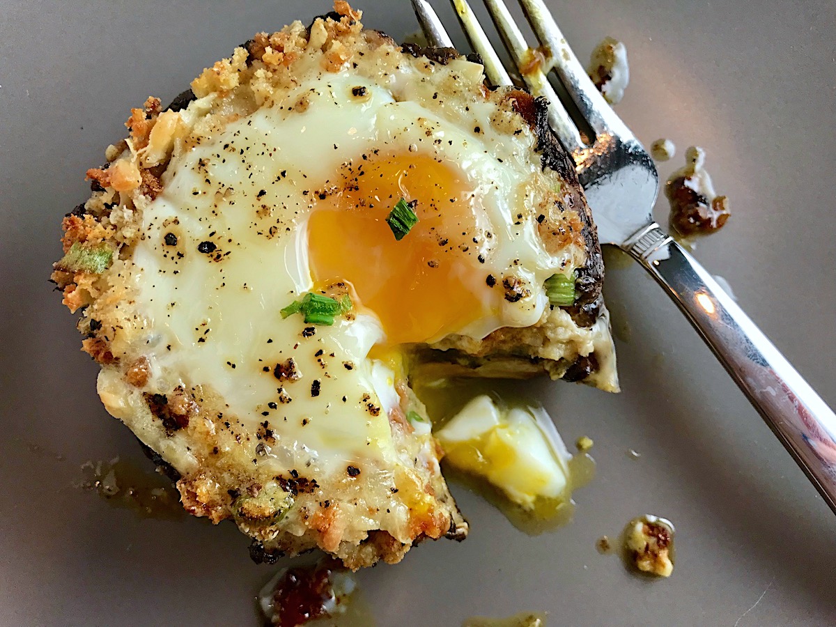 Breakfast Stuffed Mushrooms, portabella Egg Nest, on plate with bite cut out and runny yoke and fork on plate.