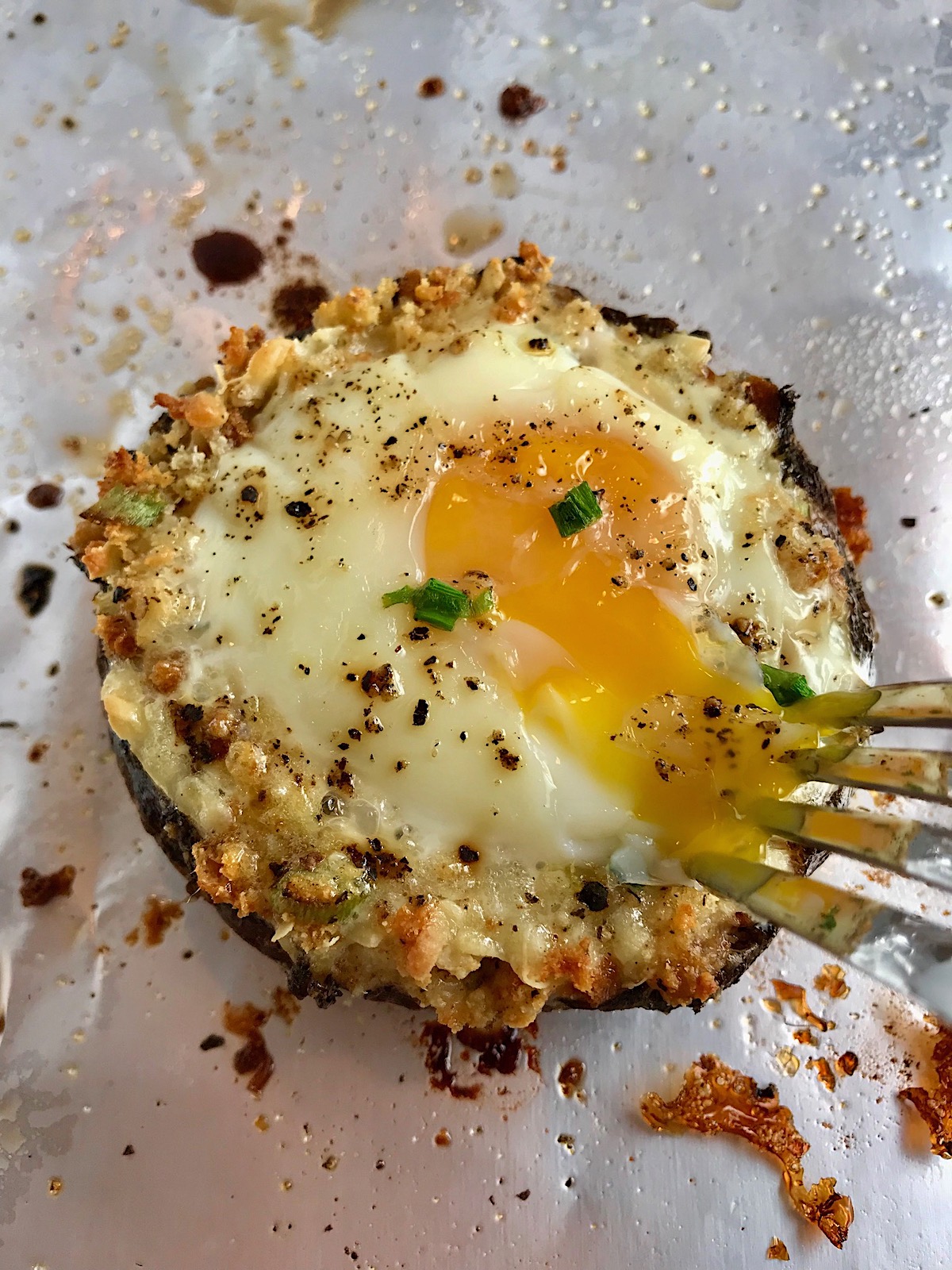 Fork poking into the yoke of Breakfast Stuffed Mushrooms, portabella Egg Nest, on pan with crispy cheesy breadcrumbs.