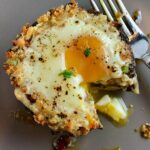 Breakfast Stuffed Mushrooms, portabella Egg Nest, on plate with bite cut out and runny yoke and fork on plate.