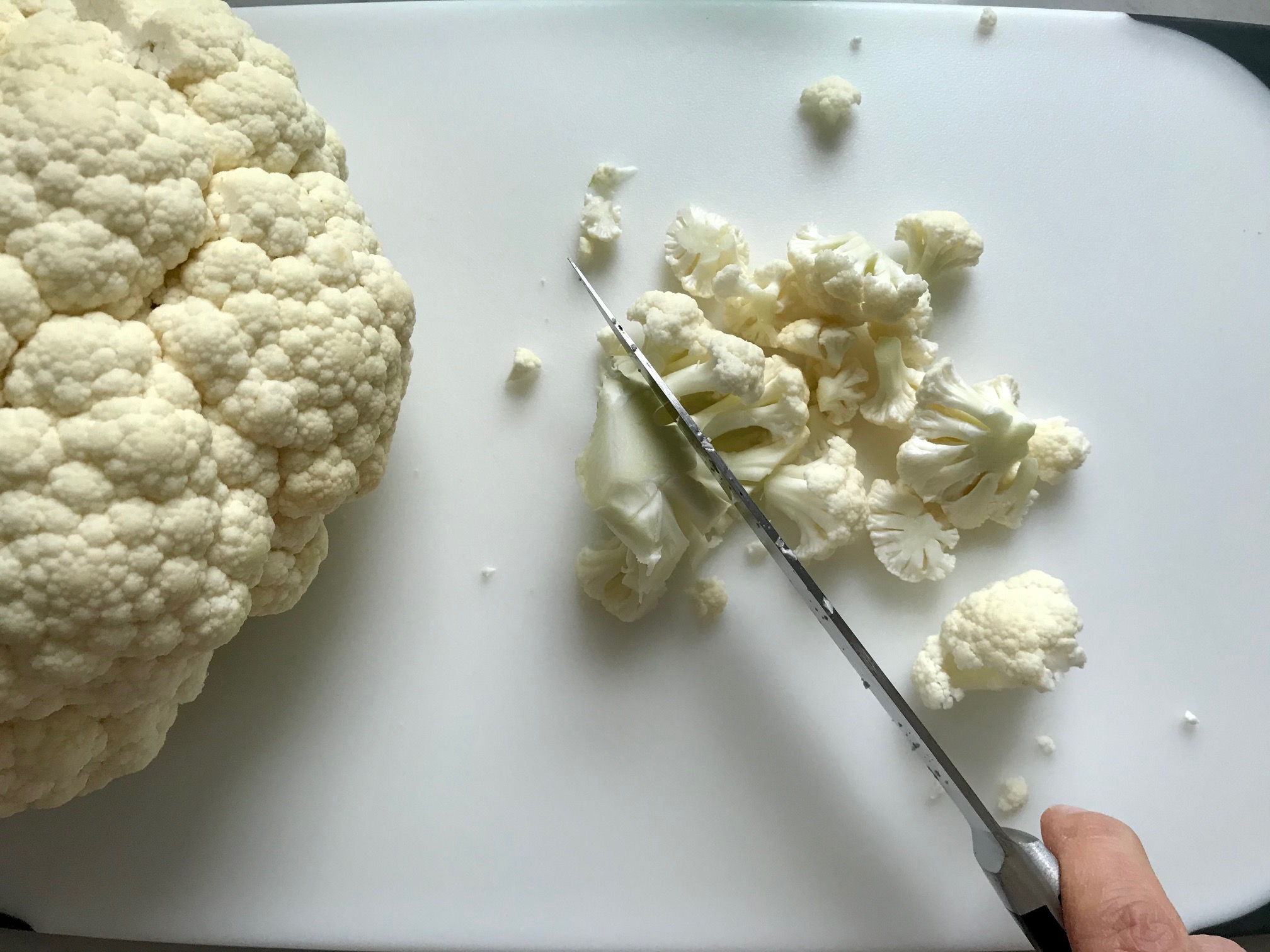 Knife cutting Cauliflower pieces on a cutting board for Creamy Cajun Cauliflower and Beans.