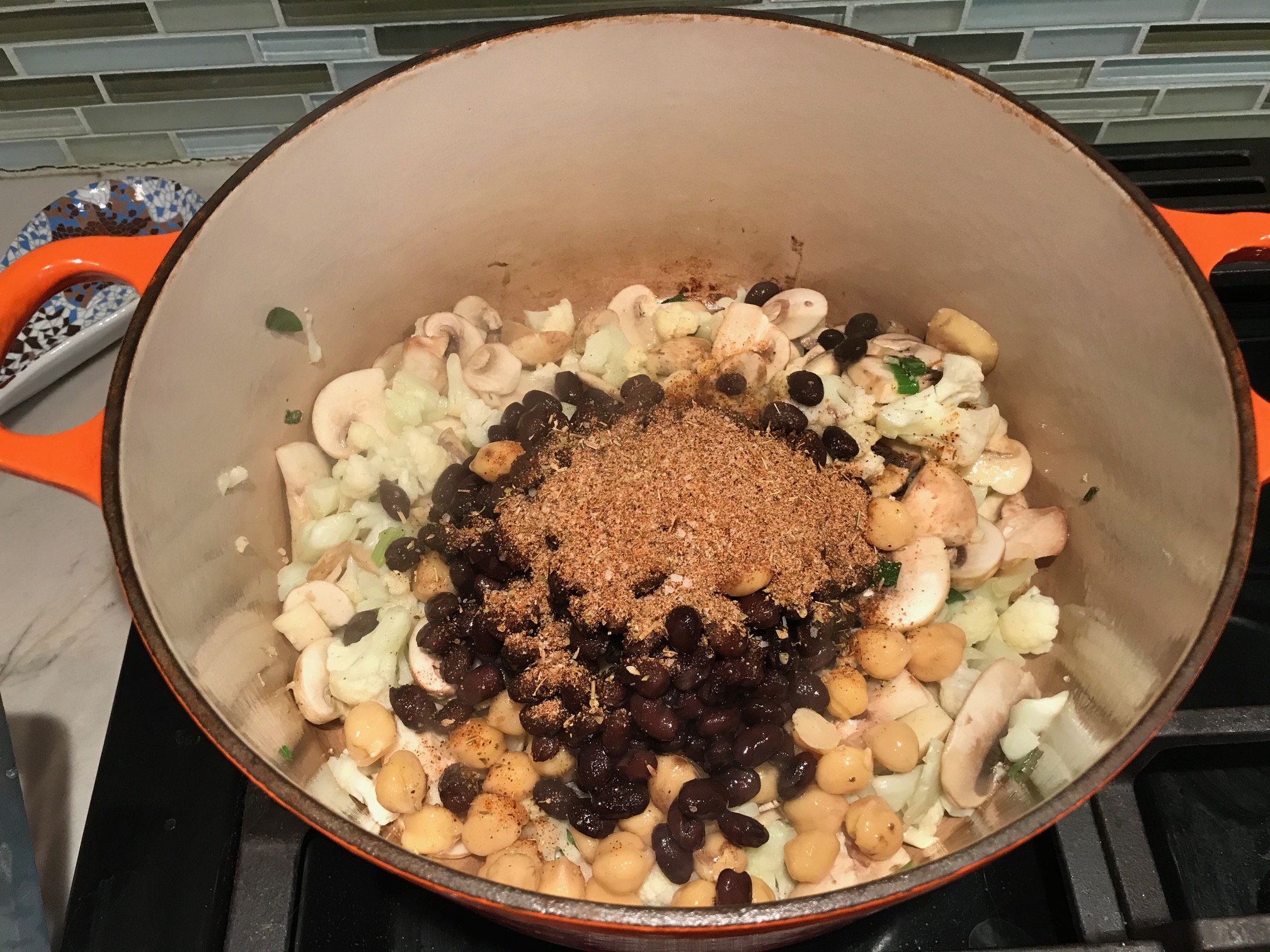 Beans and cajun seasoning added to cauliflower and mushrooms in a pot for Creamy Cajun Cauliflower and Beans.