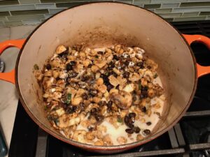 Flour, milk, broth added to beans, cajun seasoning, cauliflower and mushrooms in a pot for Creamy Cajun Cauliflower and Beans.