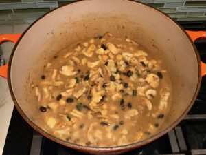 Creamy Cajun Cauliflower and Beans in a pot with wood spoon. The mild cajun flavors combined with healthy garbanzo beans, black beans, cauliflower, and mushrooms make this a hearty, creamy, and delicious dish