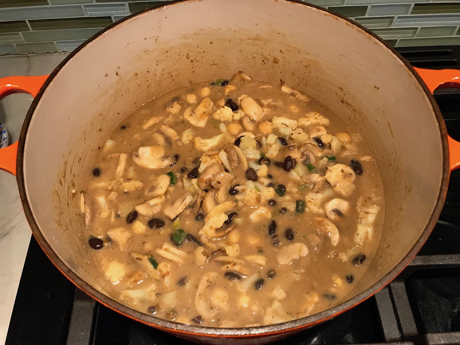 Creamy Cajun Cauliflower and Beans in a pot with wood spoon. The mild cajun flavors combined with healthy garbanzo beans, black beans, cauliflower, and mushrooms make this a hearty, creamy, and delicious dish