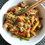 Ginger Teriyaki Tofu bowl with noodles, zucchini strips, red peppers, sesame seeds and chopsticks in the bowl.