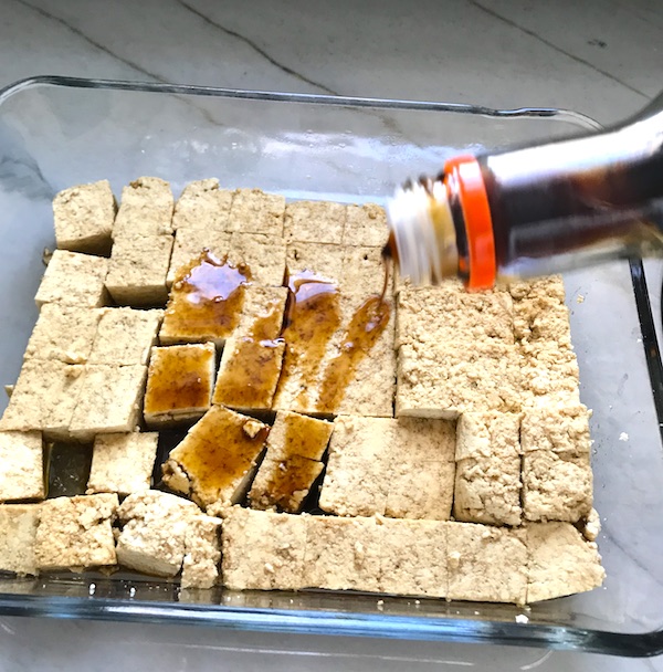 Tofu marinating in teriyaki sauce in glass dish for Ginger Teriyaki Tofu bowl with noodles.