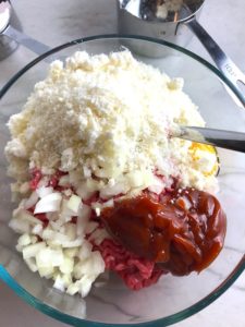 Raw ground Beef in bowl with onions, catchup, egg, and parmesan cheese on top. This 5-Ingredient Easy Meatloaf recipe may be short on ingredients, but it is loaded with flavor. The lack of breadcrumbs means you don't have them soaking up the juices, so the meat stays moist - and it's gluten free too! Parmesan cheese, onion, egg, ketchup, salt, and pepper are all that go into this yummy loaf of goodness!