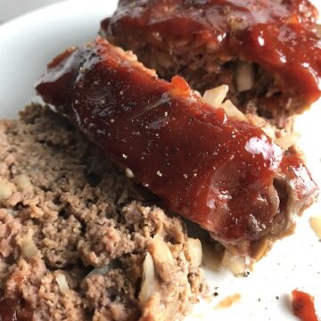 Close up picture of sliced meatloaf with ketchup on top. This 5-Ingredient Easy Meatloaf recipe may be short on ingredients, but it is loaded with flavor. The lack of breadcrumbs means you don't have them soaking up the juices, so the meat stays moist - and it's gluten free too! Parmesan cheese, onion, egg, ketchup, salt, and pepper are all that go into this yummy loaf of goodness!