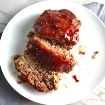 Overhead picture of sliced meatloaf with ketchup on top on a plate. This 5-Ingredient Easy Meatloaf recipe may be short on ingredients, but it is loaded with flavor. The lack of breadcrumbs means you don't have them soaking up the juices, so the meat stays moist - and it's gluten free too! Parmesan cheese, onion, egg, ketchup, salt, and pepper are all that go into this yummy loaf of goodness!