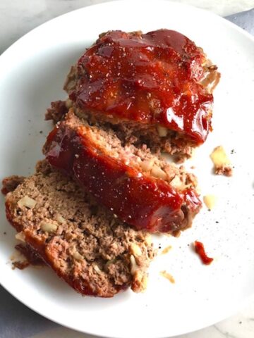 Overhead picture of sliced meatloaf with ketchup on top on a plate. This 5-Ingredient Easy Meatloaf recipe may be short on ingredients, but it is loaded with flavor. The lack of breadcrumbs means you don't have them soaking up the juices, so the meat stays moist - and it's gluten free too! Parmesan cheese, onion, egg, ketchup, salt, and pepper are all that go into this yummy loaf of goodness!