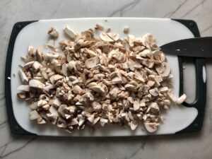 Chopped white button mushrooms on a cutting board for Creamy Parmesan Mushroom Quinoa Risotto.