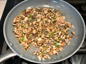 Chopped white button mushrooms cooking in a frying pan with scallions for Creamy Parmesan Mushroom Quinoa Risotto.
