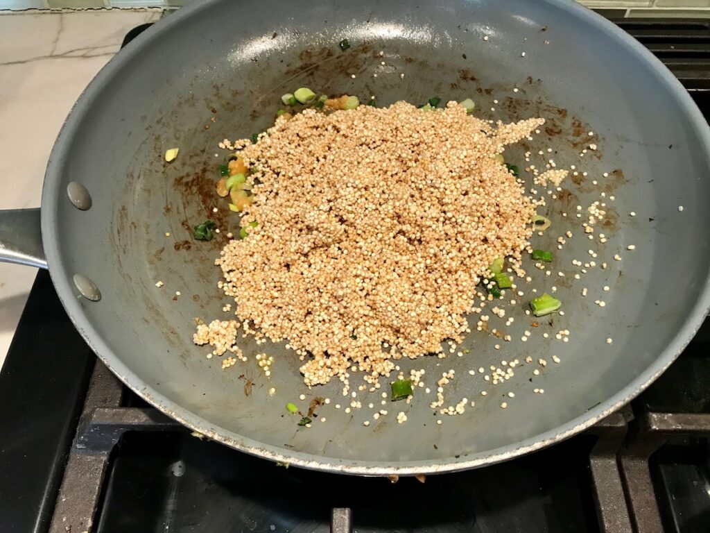 Uncooked white quinoa added to frying pan with scallions and garlic for Creamy Parmesan Mushroom Quinoa Risotto