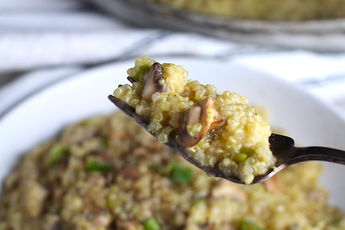 Fork with Creamy Parmesan Mushroom Quinoa Risotto bite over a bowl and skillet in background. This recipe has the traditional garlic flavor in the background and the nuttiness from the Parmesan combined with the meaty earthy flavor of the mushrooms. There is no wine.