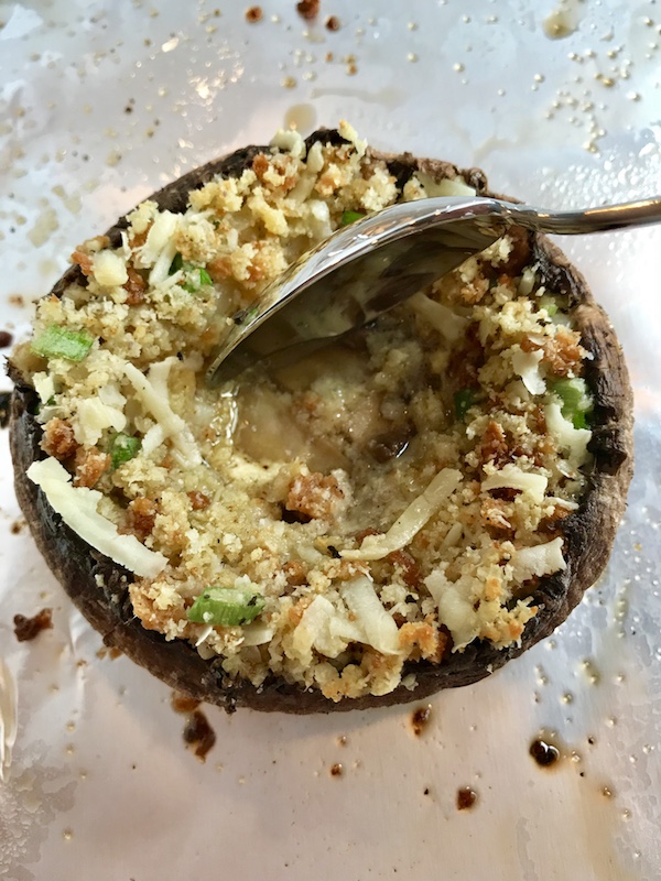 Spoon pressing in the filling in the Portabella Mushroom Egg Nests on pan. Portabella mushrooms are filled with garlic, scallion, breadcrumb & Manchego cheese stuffing! Then an egg is baked nestled in the center of all of this goodness.