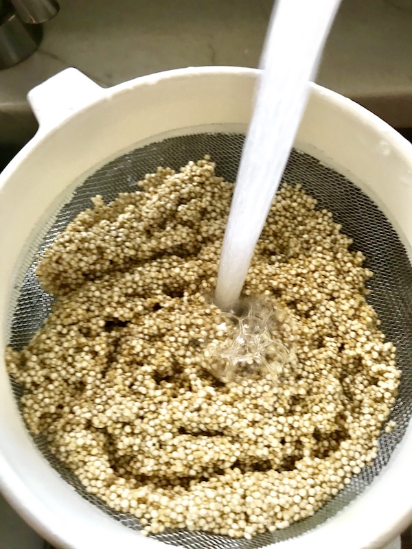 Quinoa in strainer with water pouring over to rinse it.