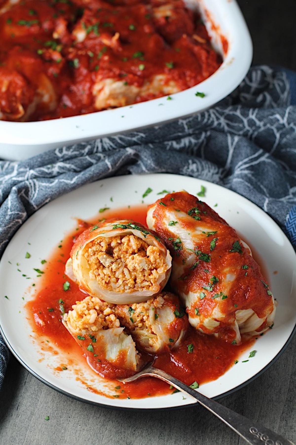 Stuffed Cabbage Rolls on a plate with one cut open. They're a great make-ahead family dish! This recipe uses ground chicken, paprika, parmesan, tomato paste, garlic, and onion for tons of flavor!