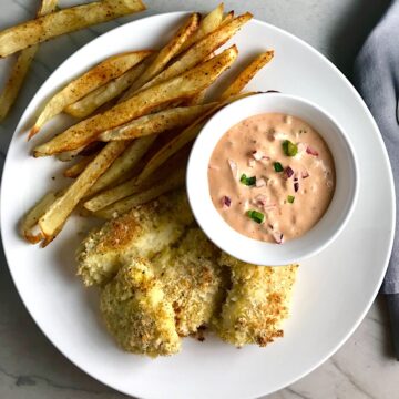 Crispy Baked Cod Panko Fish and Chips on a plate with side of remoulade dipping sauce. Everything bakes in the oven on a sheet pan to save time and energy.