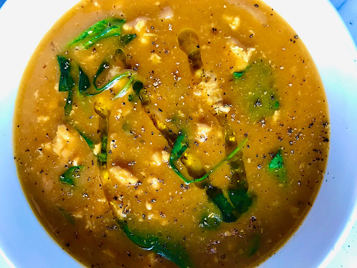 Creamy Tomato Soup with chicken in a white bowl on counter with olive oil drizzled on top.