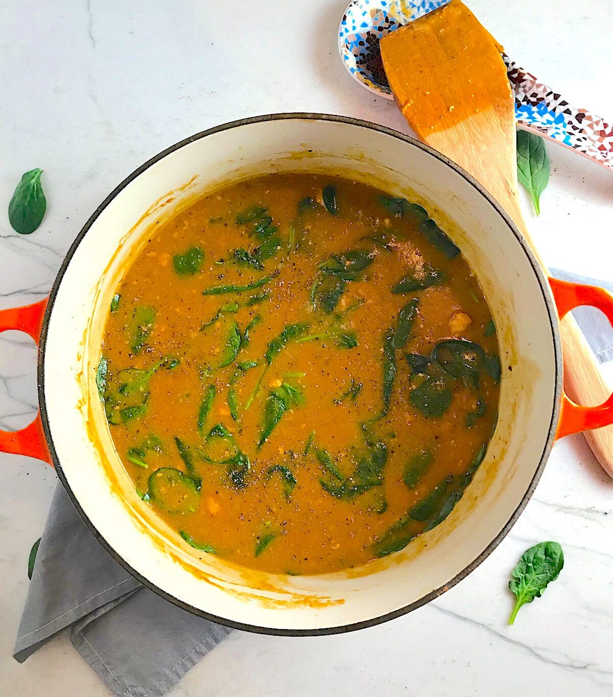 Creamy Tomato Soup with chicken and spinach in a pot on counter with wooden spatula next to it.