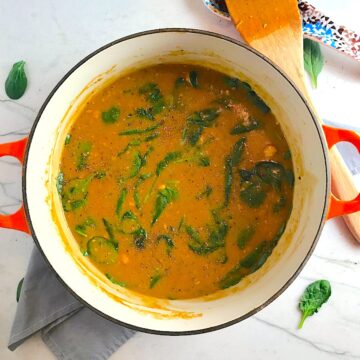 Creamy Tomato Soup with chicken and spinach in a pot on counter with wooden spatula next to it.