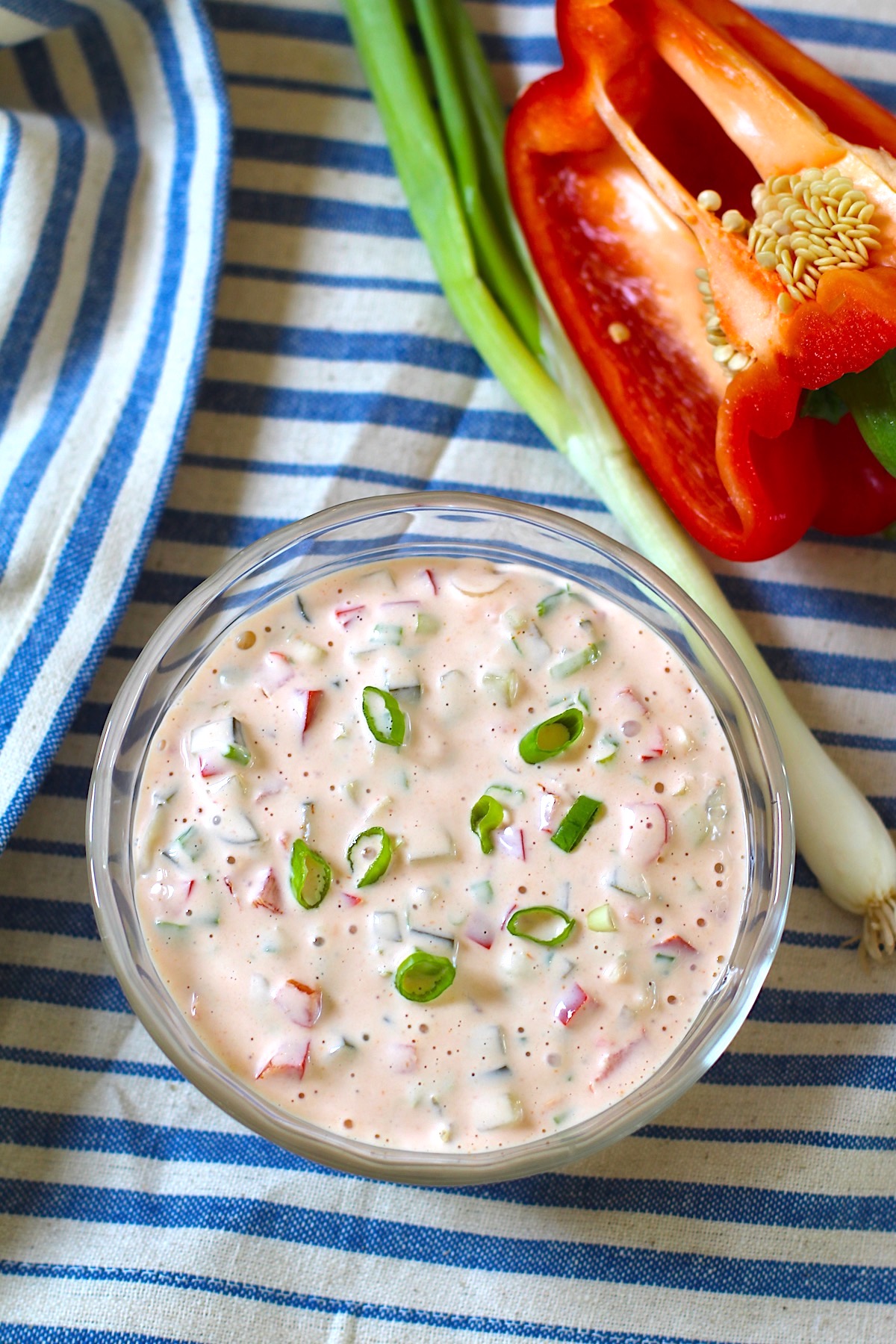 Crunchy Mayo and Ketchup dipping sauce with pickles, red peppers, and scallions on a blue and white striped towel with whole scallion and cut red pepper sitting next to it.
