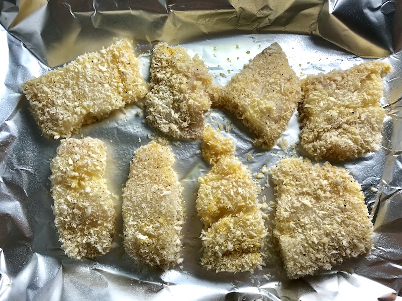 Raw cod fish breaded on a sheet pan lined with aluminum before being baked for Crispy Baked Cod Panko Fish and Chips.