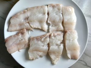 Raw cod fish cut into large pieces on a plate for Crispy Baked Cod Panko Fish and Chips.